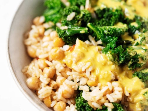 A serving bowl holds colorful plant-based ingredients, dressed in a golden, creamy sauce.