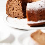 A large, white plate has been topped with a round applesauce spice bundt cake. A few slices of the cake peek out in the foreground.