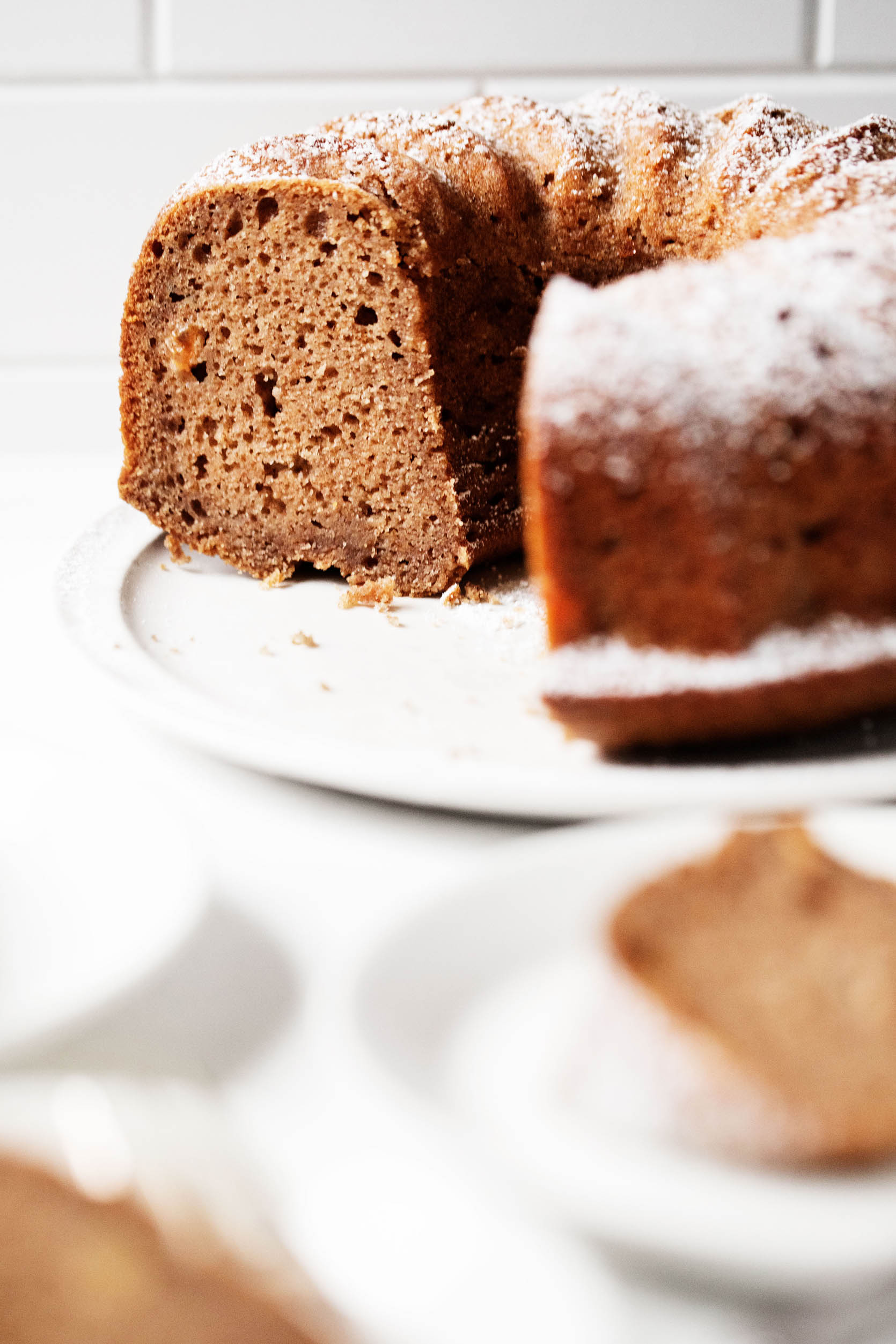 A large, white plate has been topped with a round applesauce spice bundt cake. A few slices of the cake peek out in the foreground.