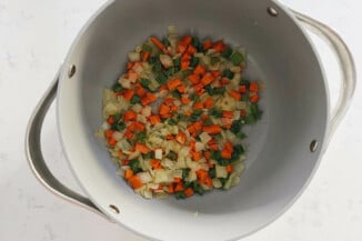Onion, carrot, and celery is being sautéed in a gray pot.