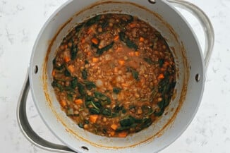 A large gray pot contains a vegan lentil soup, which also has kale in it.