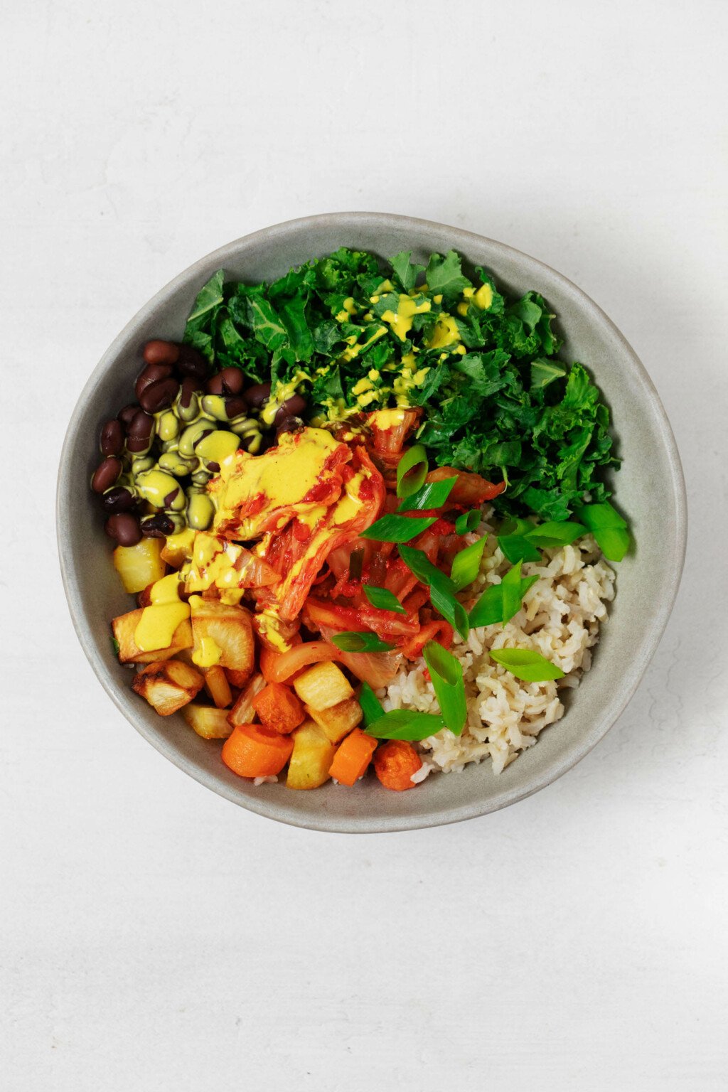 A vegan breakfast macro bowl has been topped with a bright yellow-hued sauce. The bowl is resting on a white surface.