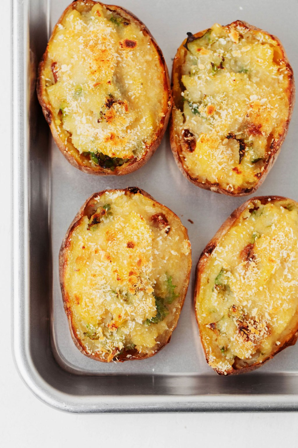 A metal baking sheet is lined with loaded, garlic kale potatoes.