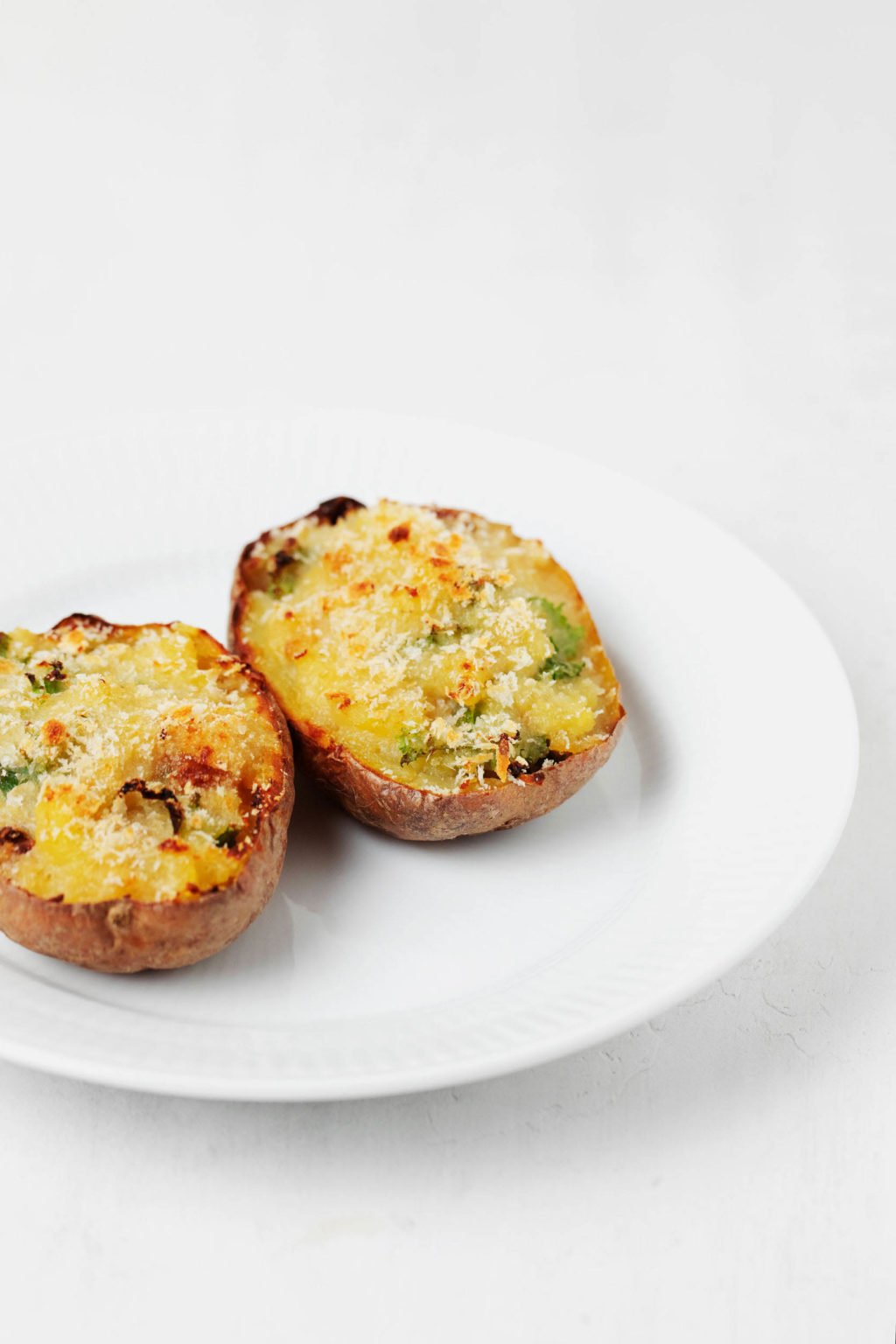 Two loaded, baked potatoes have been stuffed with kale and garlic. They rest on a round, white plate.