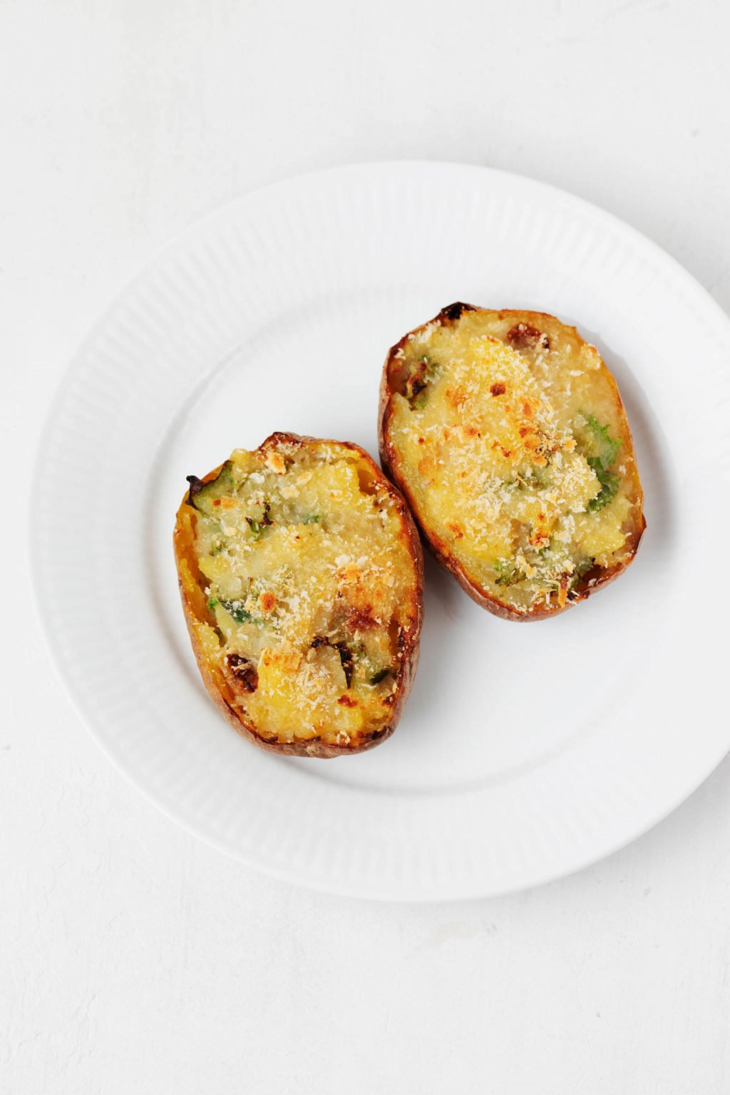 Two small baked potato halves rest on a round white plate.