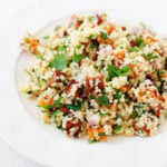 A wide-rimmed, white bowl is filled with a cooked vegan whole grain and sweet potato salad with herbs.