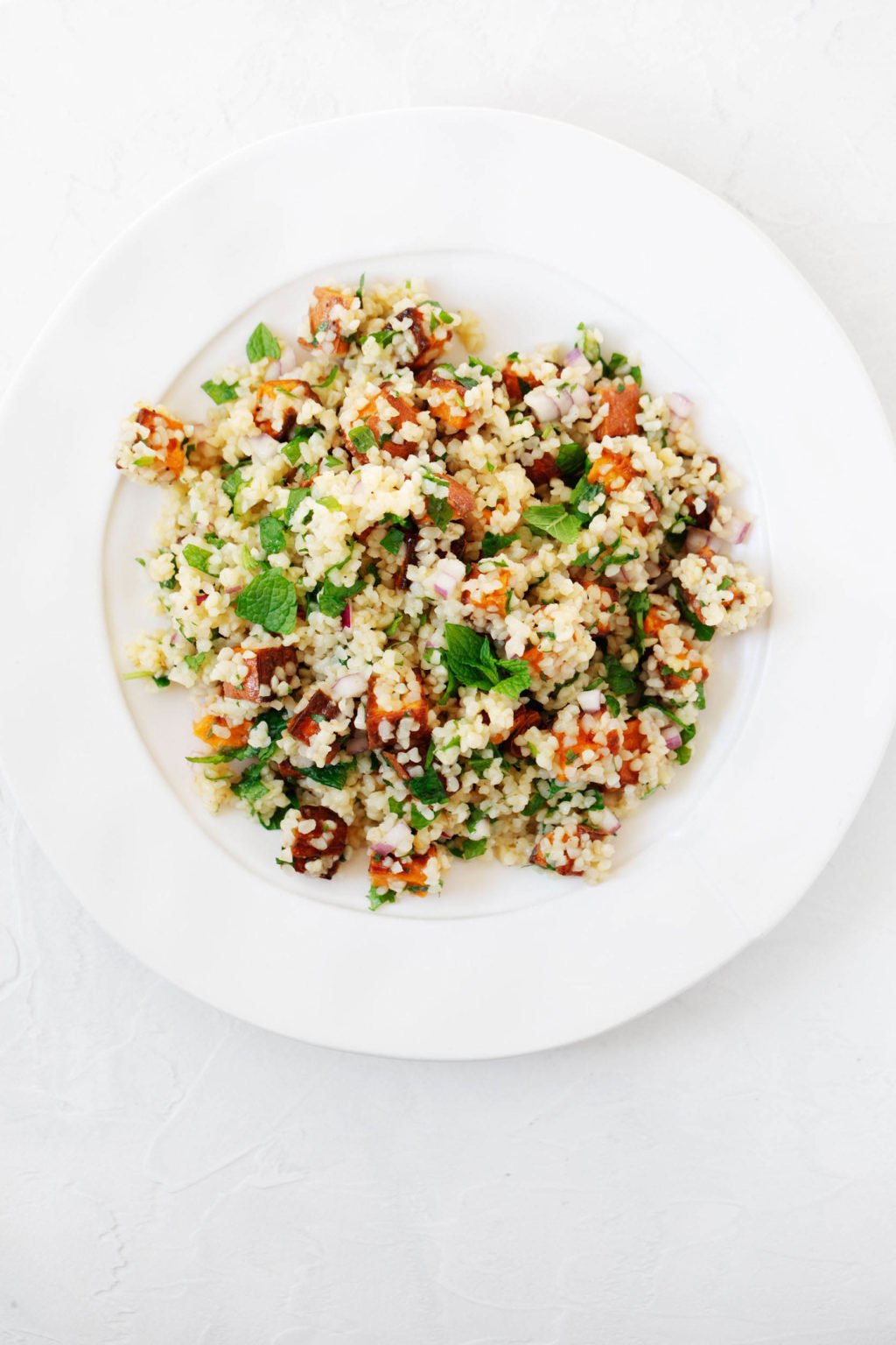 An overhead image of a wide, round plate against a white backdrop. The plate holds a vegan whole grain salad.