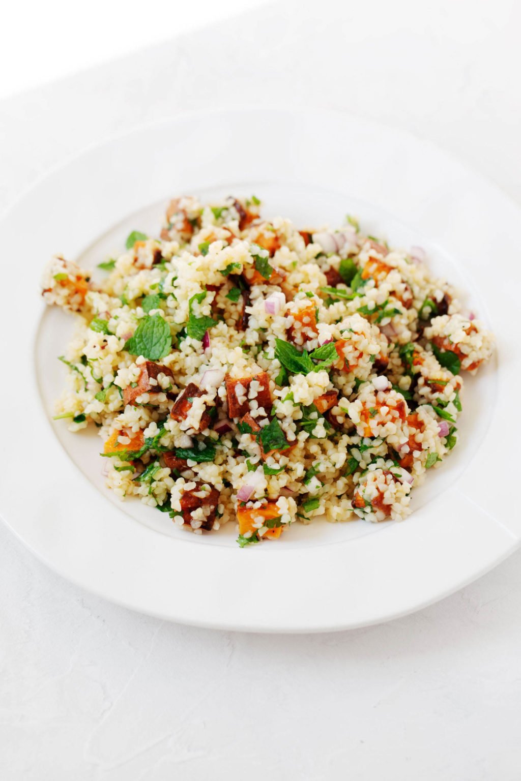 An angled photo of a vegan bulgur sweet potato salad, which has been piled into a shallow, round bowl.