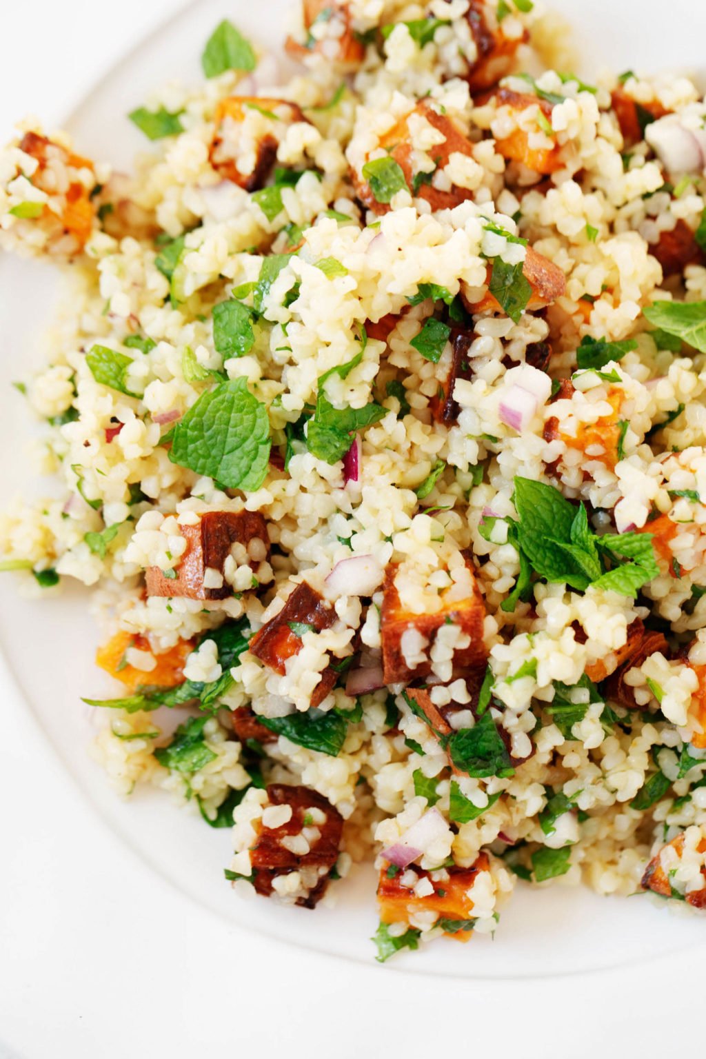 A close up image of a bulgur sweet potato grain salad, which is topped with chopped fresh mint.