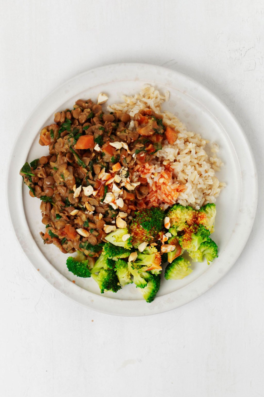 A white ceramic plate has been piled with vegetables, legumes, and brown rice. It rests on a white surface.