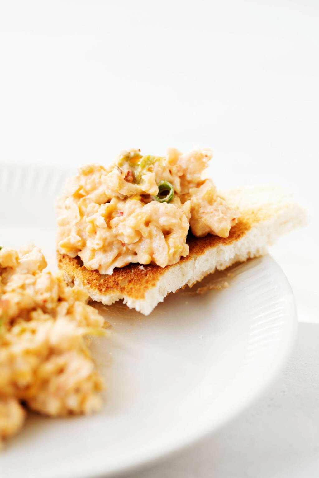 A torn slice of toast, topped with legumes, is resting on the rim of a small white plate.