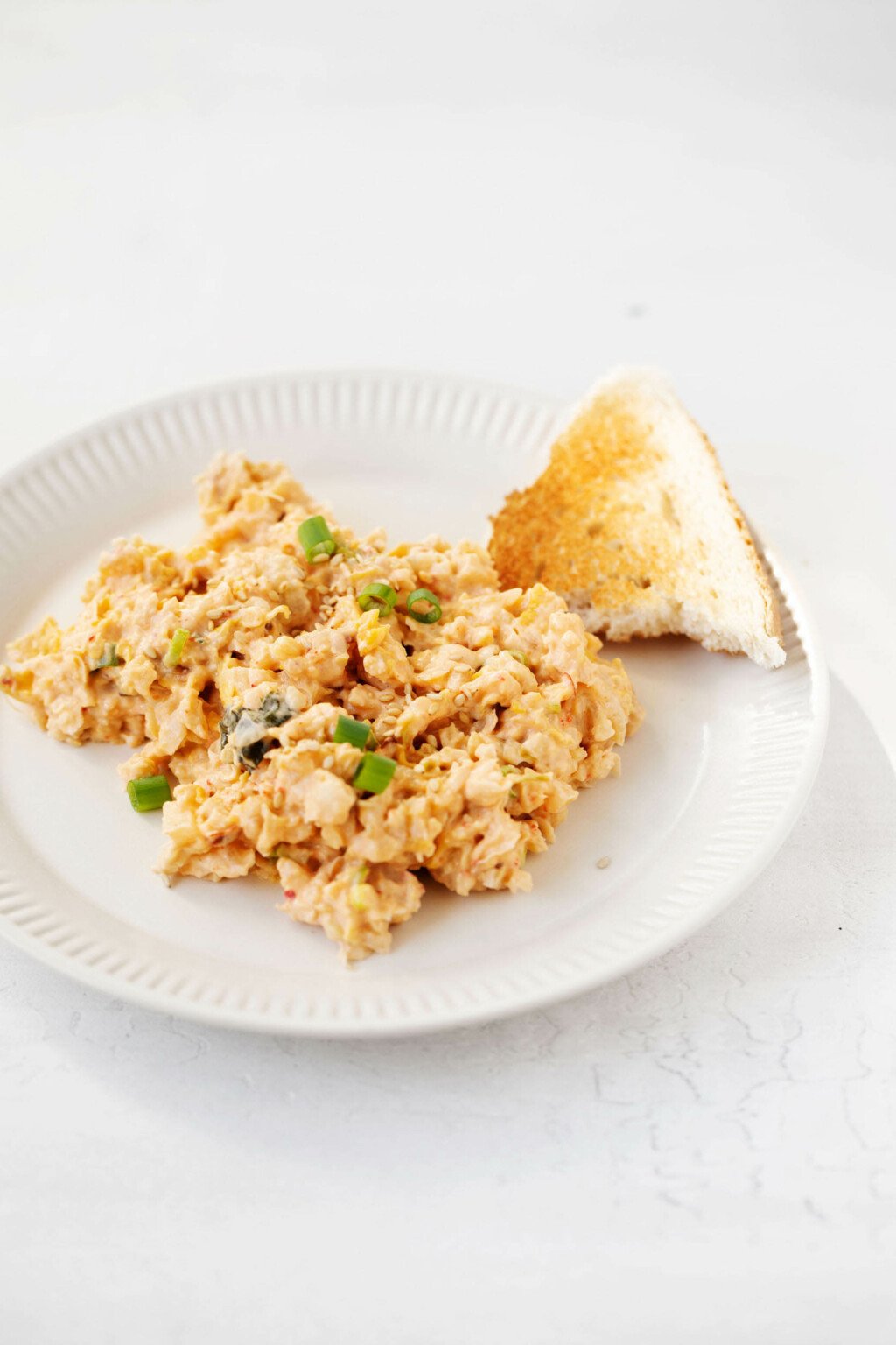 A creamy bean salad has been served on a round, white, rimmed plate. A small toast point is laying nearby, for scooping up the beans.