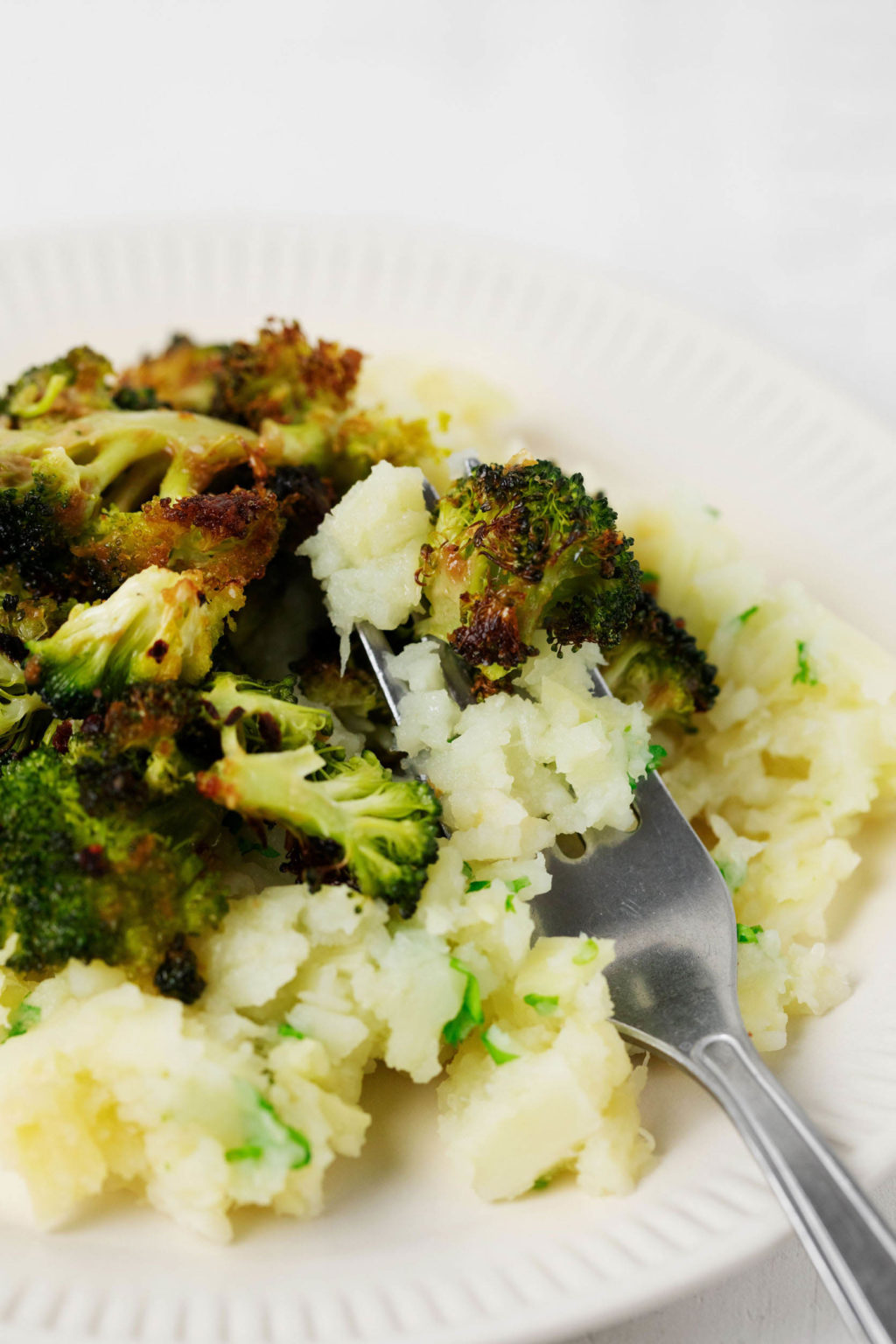 A zoomed in photo of roasted and browning broccoli, served with vegetables and herbs.