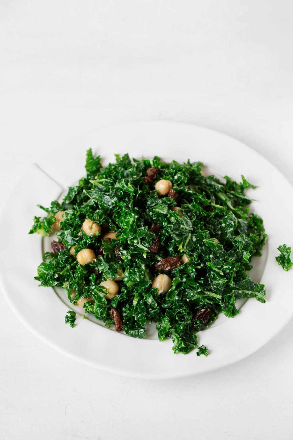 A white serving plate, piled high with greens, raisins, and legumes, rests on a white surface.