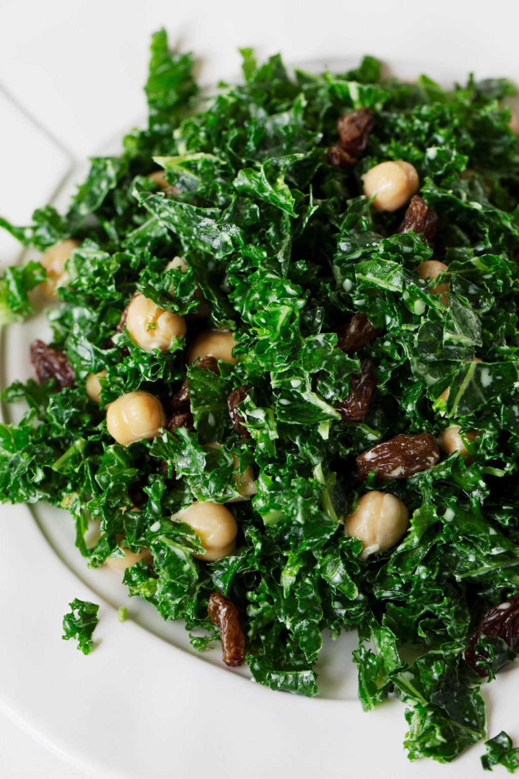 A close-up photograph of a tahini mint kale salad, which is studded with cooked chickpeas and raisins.