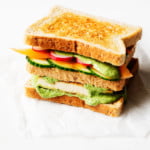 A colorful, three layered vegan green goddess sandwich is placed on a small piece of parchment paper, waiting to be cut in half.