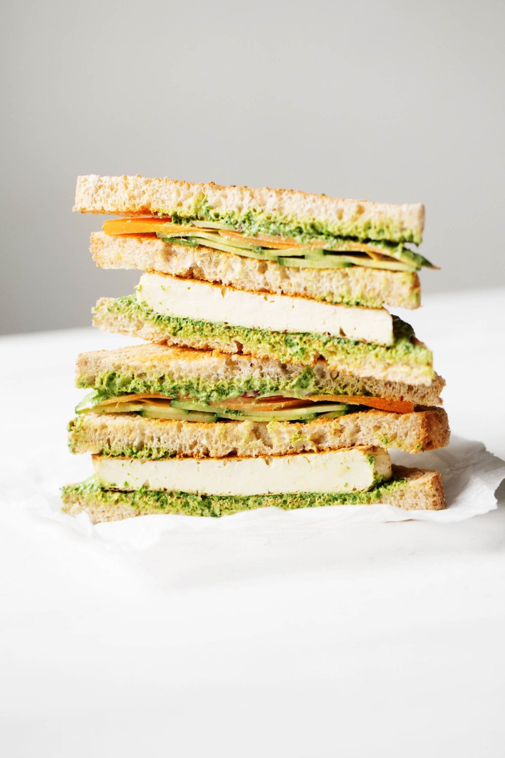 A vegan club sandwich has been sliced in half and stacked. It's filled with grilled tofu and a green sauce.