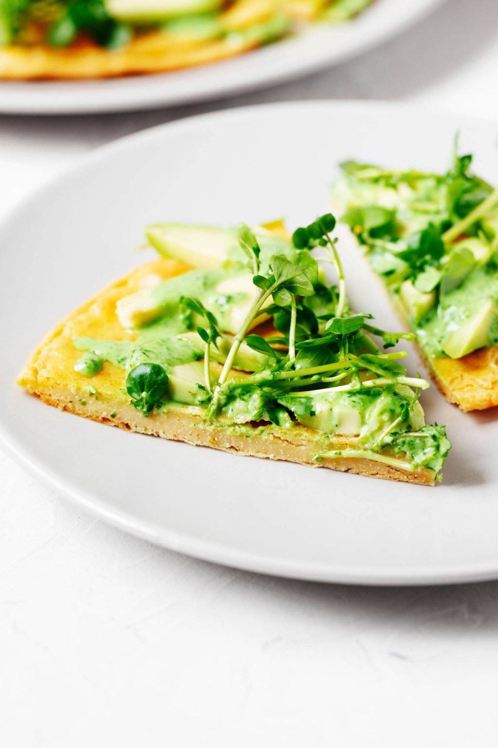 Two slices of green goddess spring socca, a socca recipe made with fresh greens and a creamy herb dressing, are on a small serving plate.