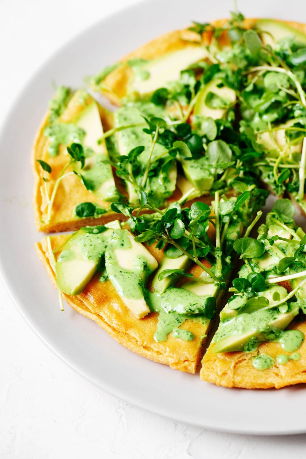 A chickpea pancake has been topped with vibrant spring greens and a creamy, green herb sauce.