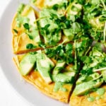 A chickpea pancake has been topped with vibrant spring greens and a creamy, green herb sauce.