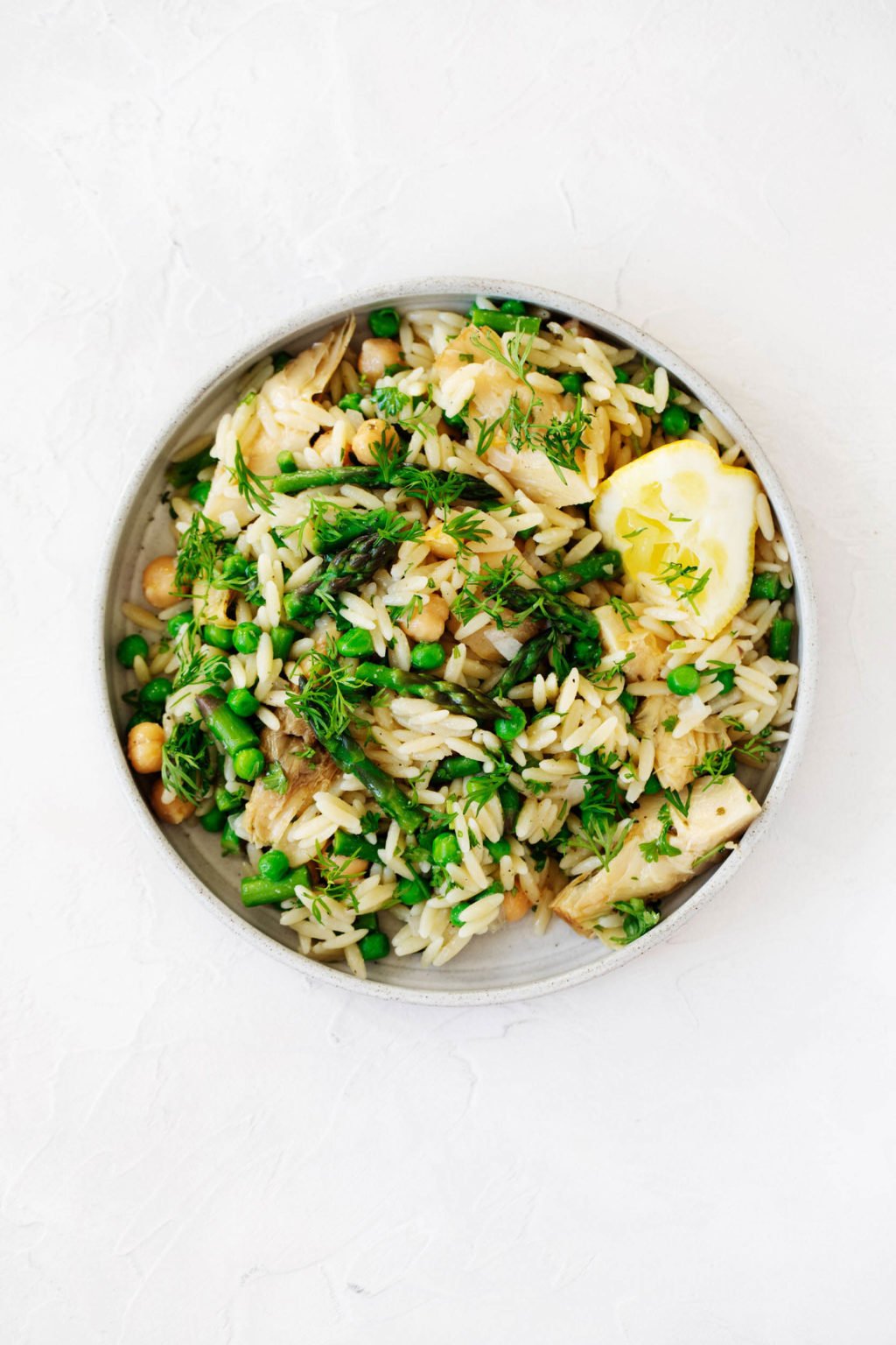 An overhead photograph of a round, white rimmed plate, which serves a plant-based salad piled with green vegetables.