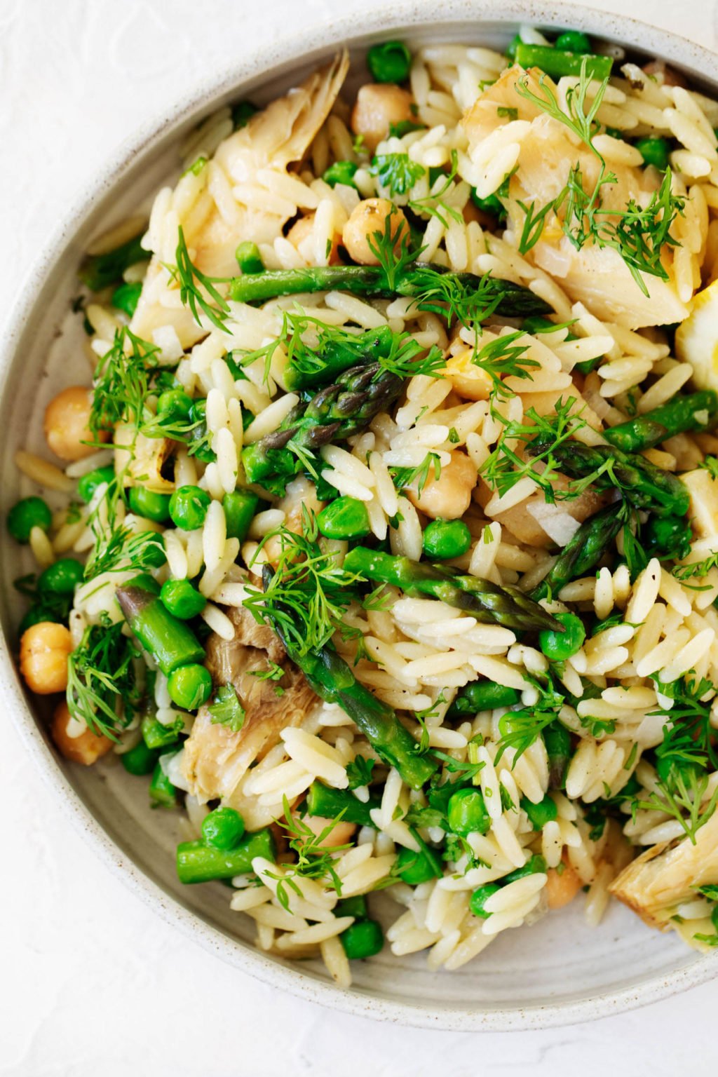 A white, rimmed, round serving plate holds a verdant, seasonal plant-based dish. Green peas and chopped dill have been used as garnish.