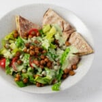 An image of a layered fattoush salad with crispy roasted chickpeas, which has been served in a shallow white bowl.