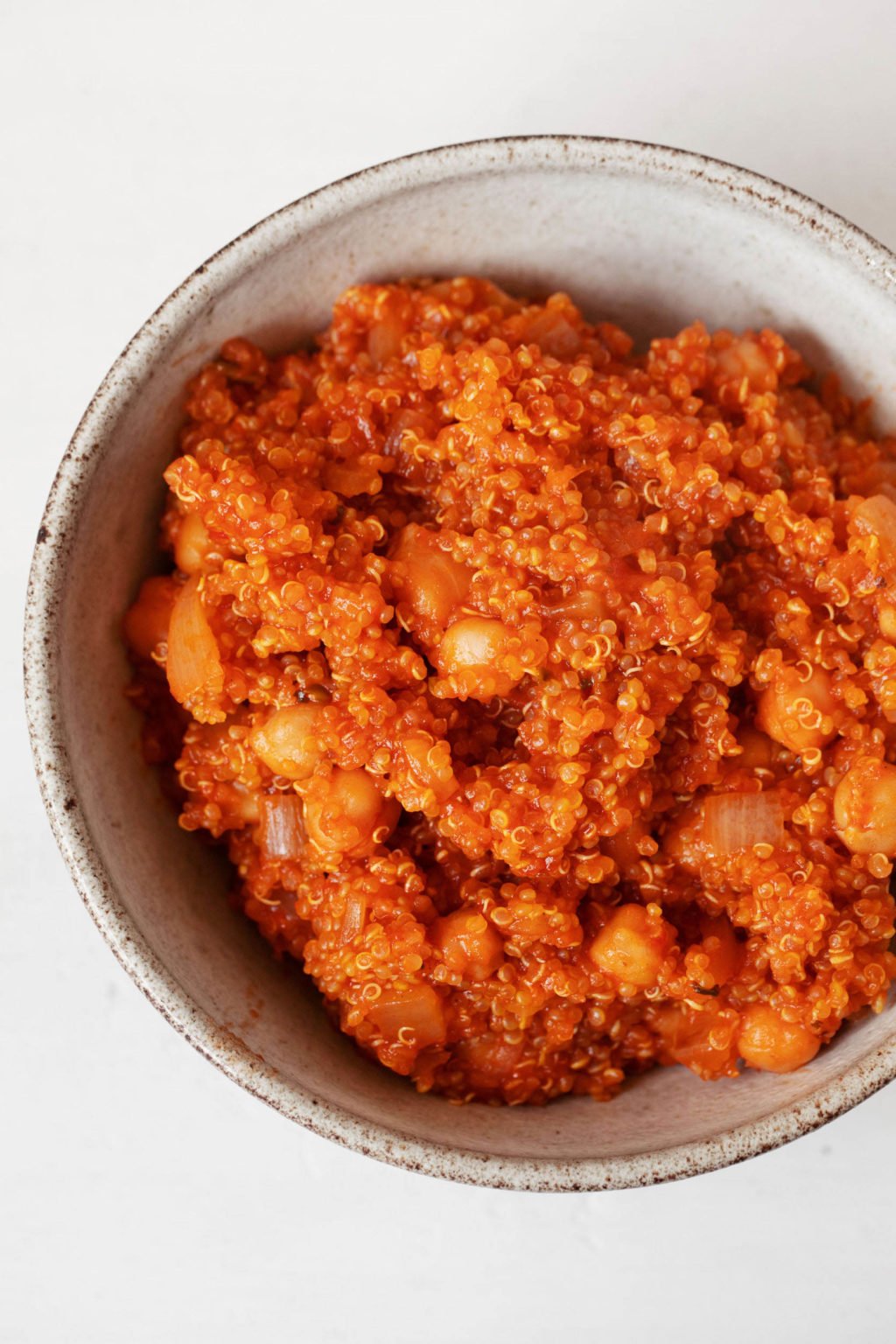 A zoomed in image of a cooked whole grain, which is a bright red color thanks to its seasoning. The grain is mixed with cooked chickpeas and served in a bowl.