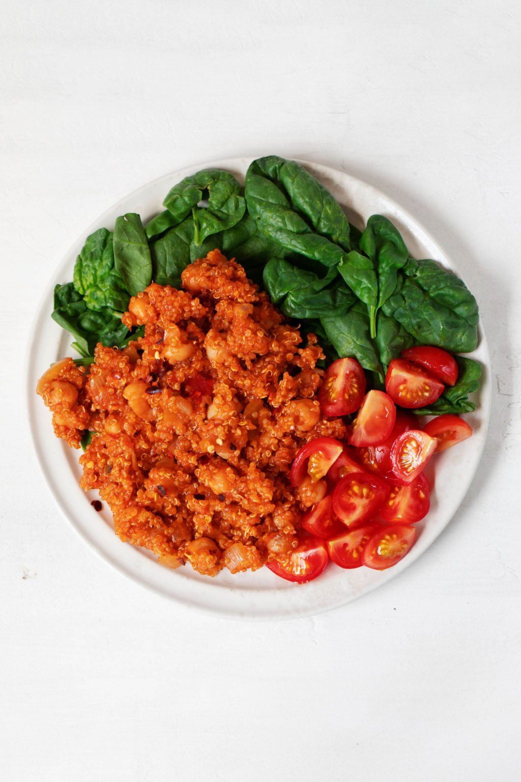 A round, white plate has been topped with grape tomatoes, baby spinach, and quinoa that has been seasoned with tomato.