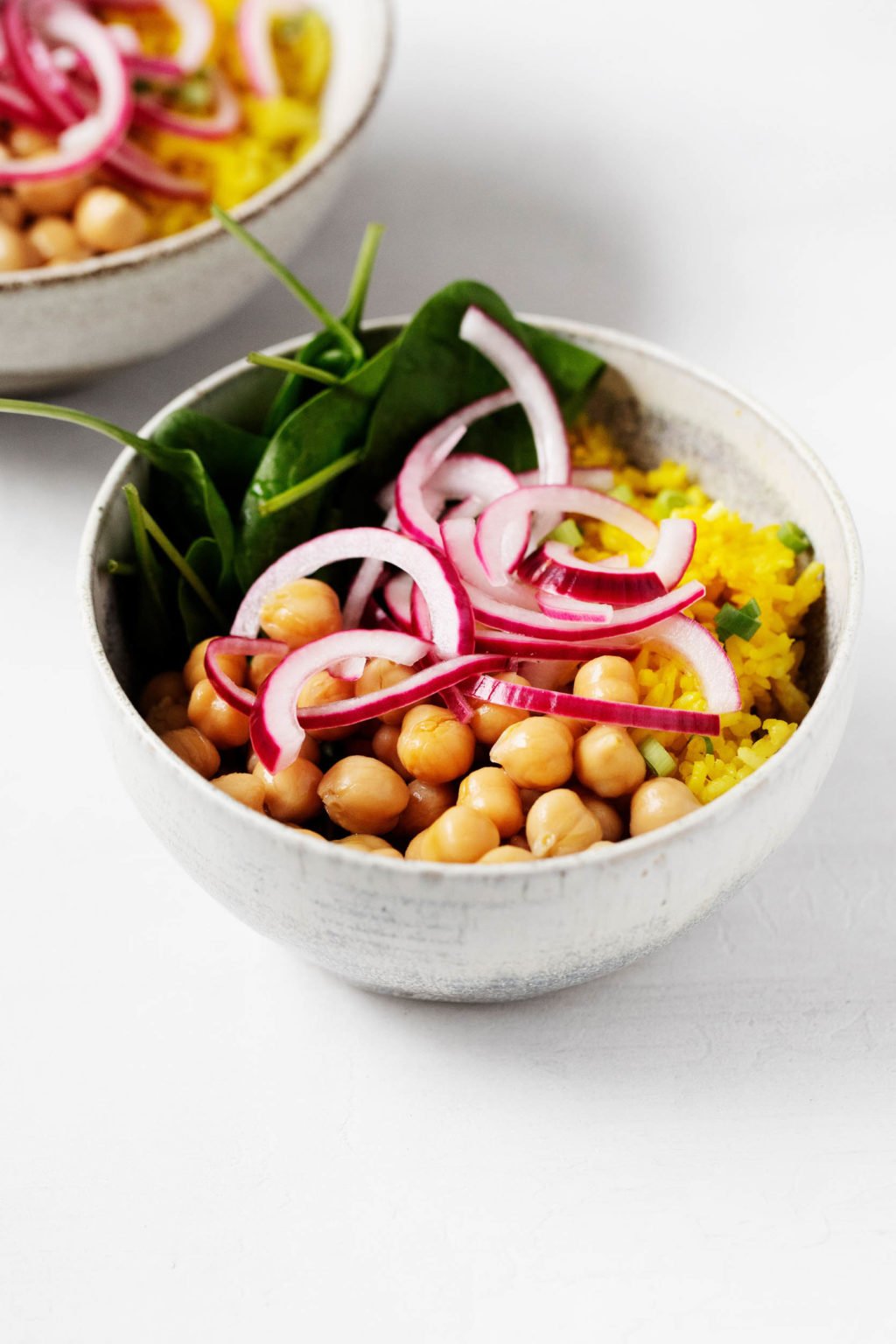 An angled photograph of two turmeric rice bowls, garnished with pink pickled onions.