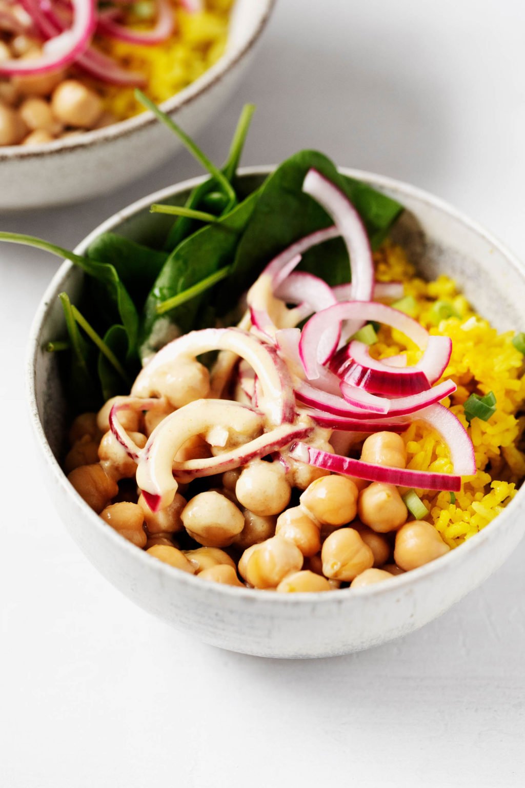 A zoomed in image of a white bowl that has been piled with spinach, onions, chickpeas, and yellow turmeric-spiced rice.