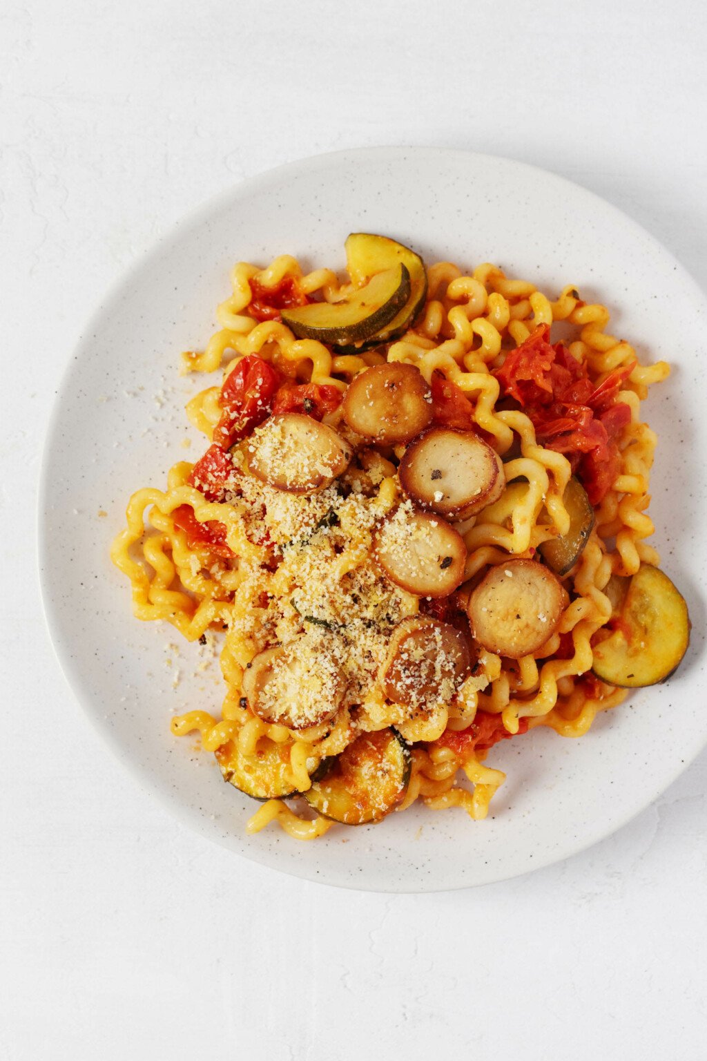 A dish of mushroom scallop pasta and bright red burst cherry tomatoes is plated on a round white plate.