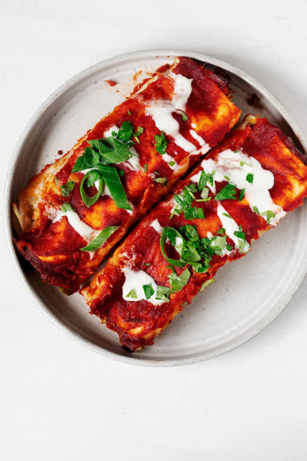 An overhead image of two enchiladas and red sauce, served in a round, white plate.