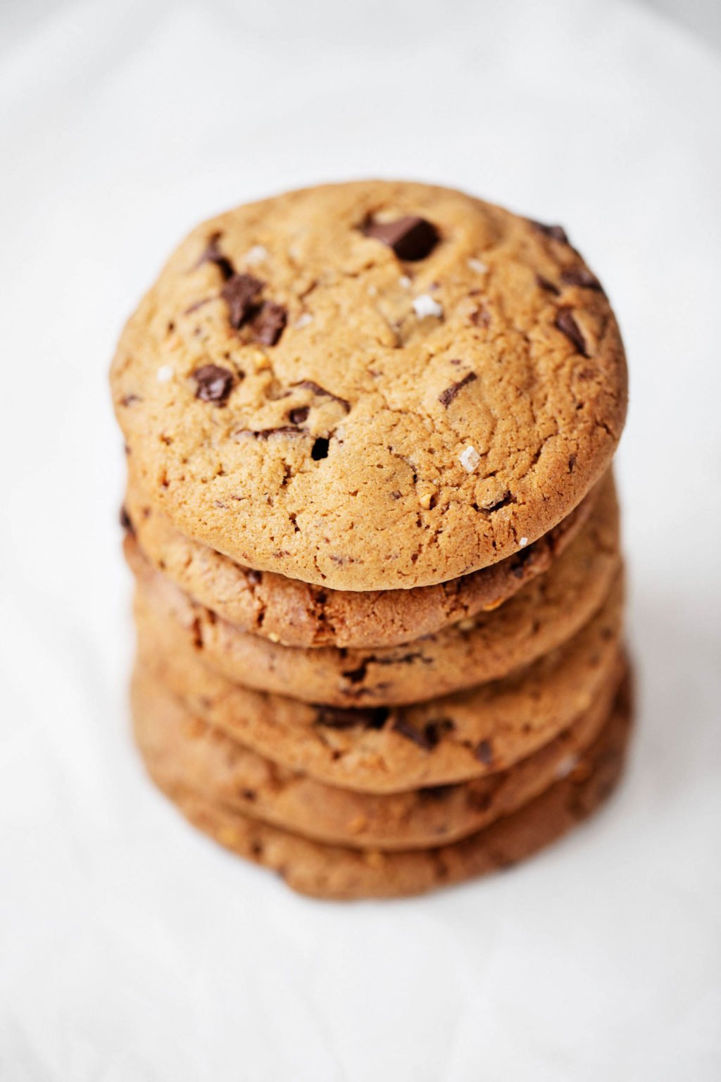 A stack of chewy, vegan chocolate chip cookies rests on a while sheet of parchment.