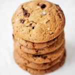 A stack of chewy, vegan chocolate chip cookies rests on a while sheet of parchment.