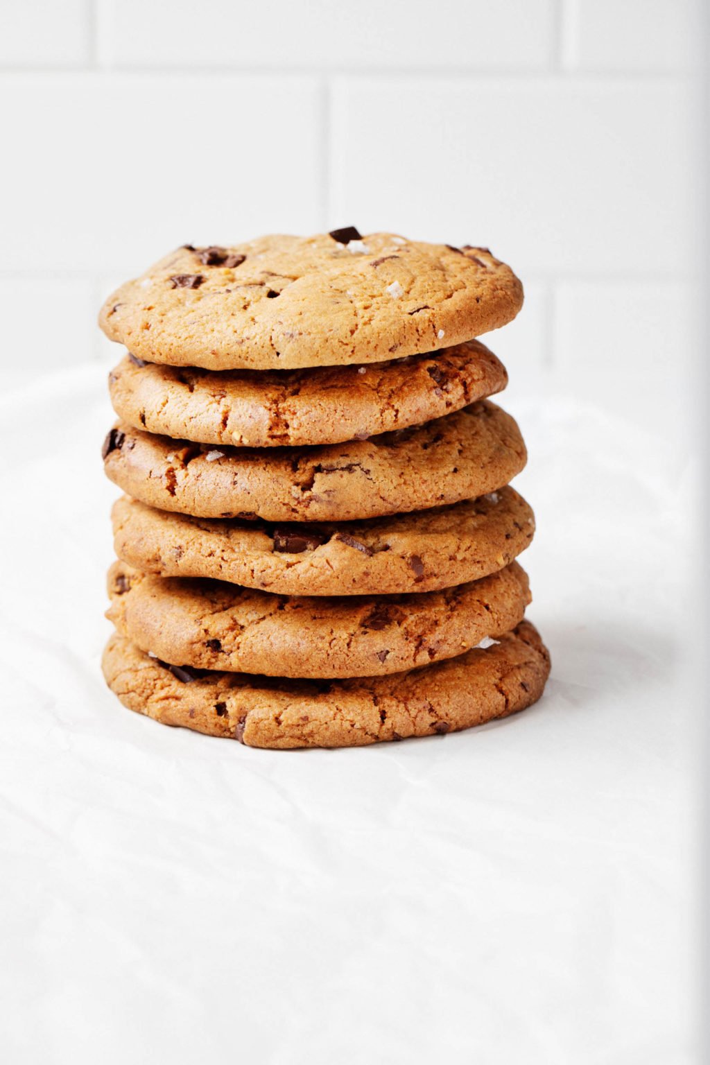 An angled photo of a stack of vegan cookies. It rests on a parchment paper sheet against a white backdrop.