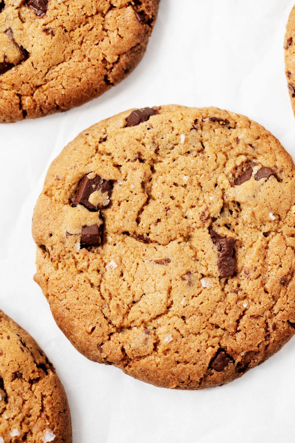 A close up, overhead photograph of vegan chocolate chip cookies placed on a white parchment surface.