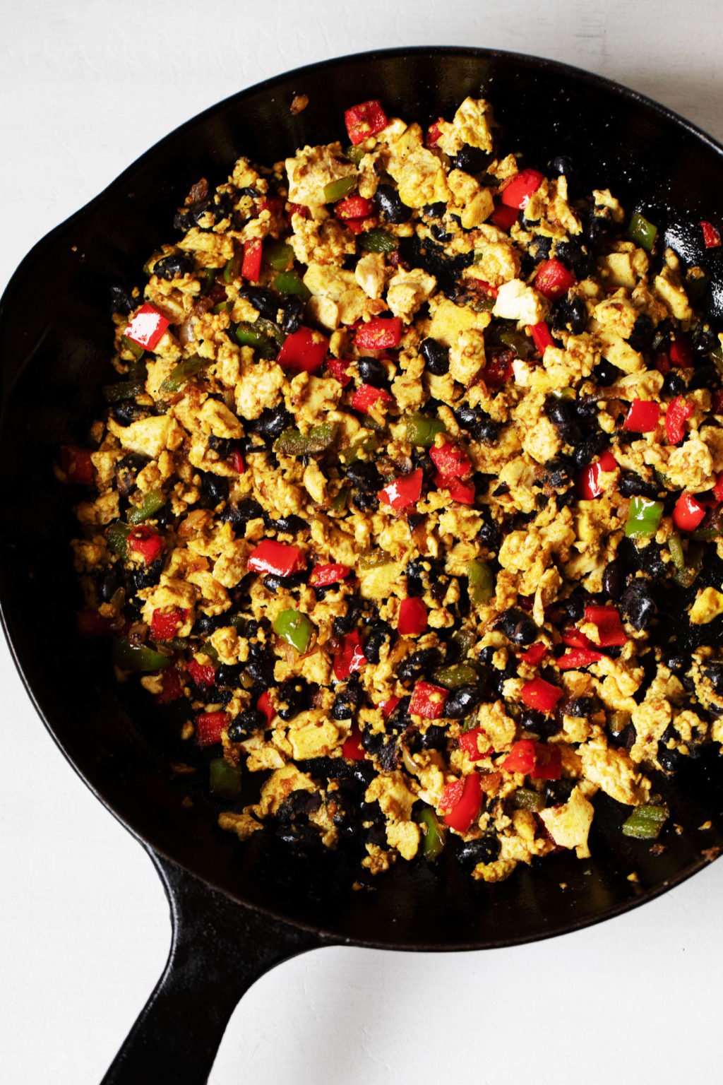 A black, cast iron skillet is filled with a mix of black beans, vegetables, and soy protein.