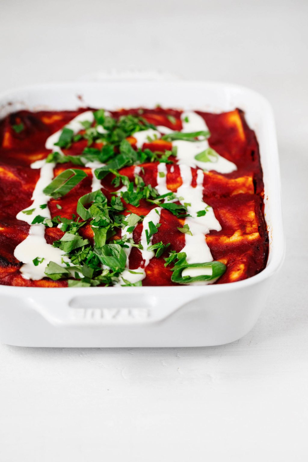 A white, rectangular baking dish holds a try full of freshly baked, tofu-stuffed vegan enchiladas. They're covered with red sauce and garnished with cilantro.