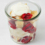 An overhead image of a mason jar that's filled with red raspberries, cubes of lemon cake, and ice cream.