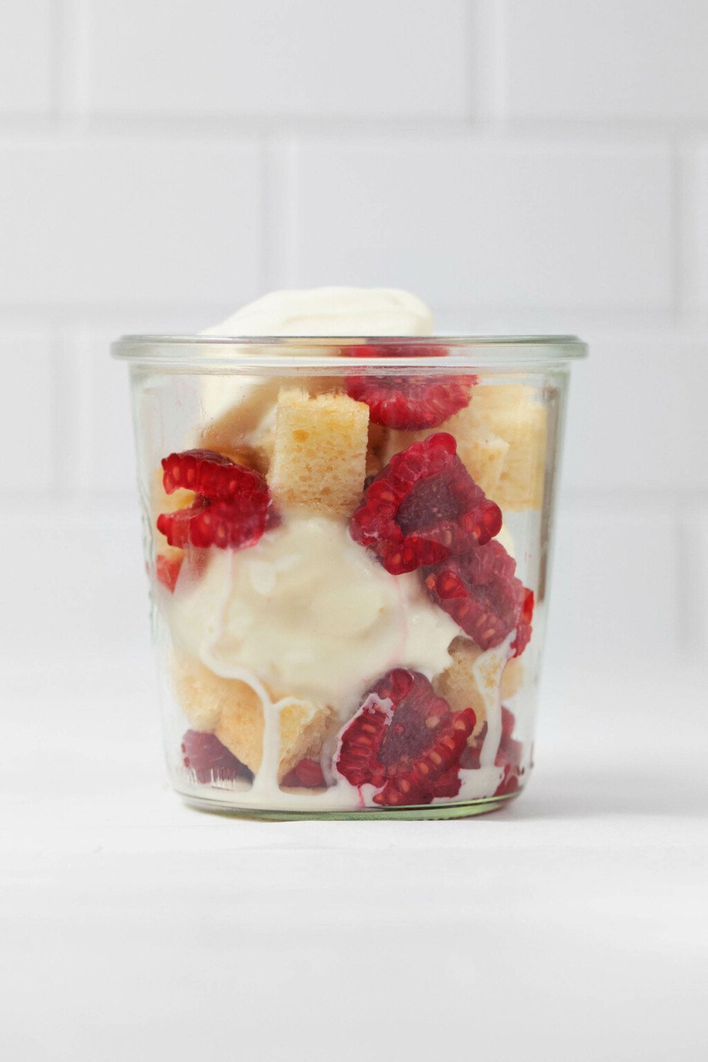 A clear, Weck mason jar holds the ingredients for a mini trifle, which is made with berries, lemon cake, and ice cream.