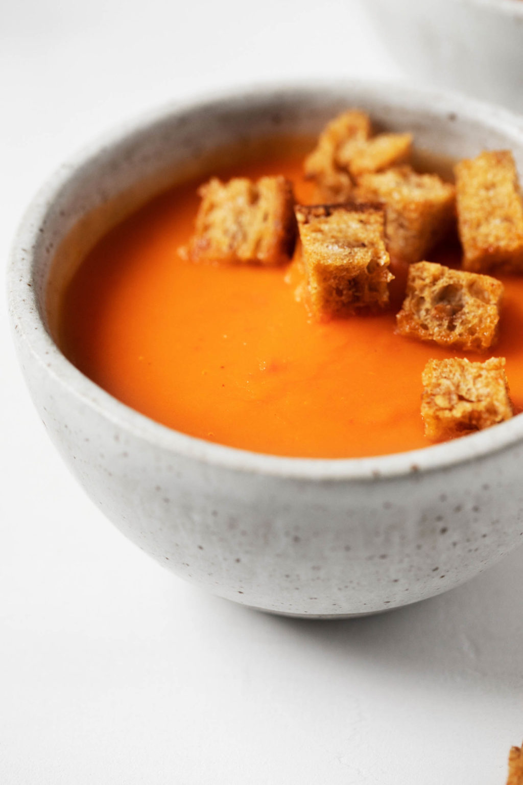 A zoomed in image of a creamy, orange hued plant-based soup, topped with crispy bread cubes.