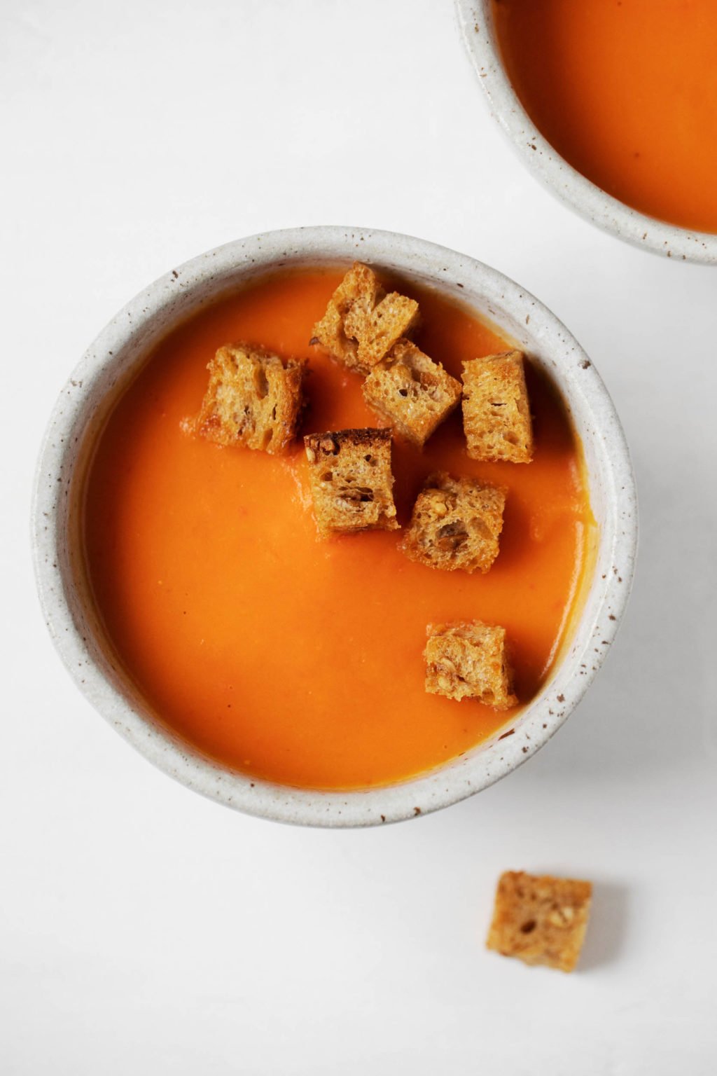 A bowl of pureed vegetable soup is topped with crispy, rustic bread croutons.