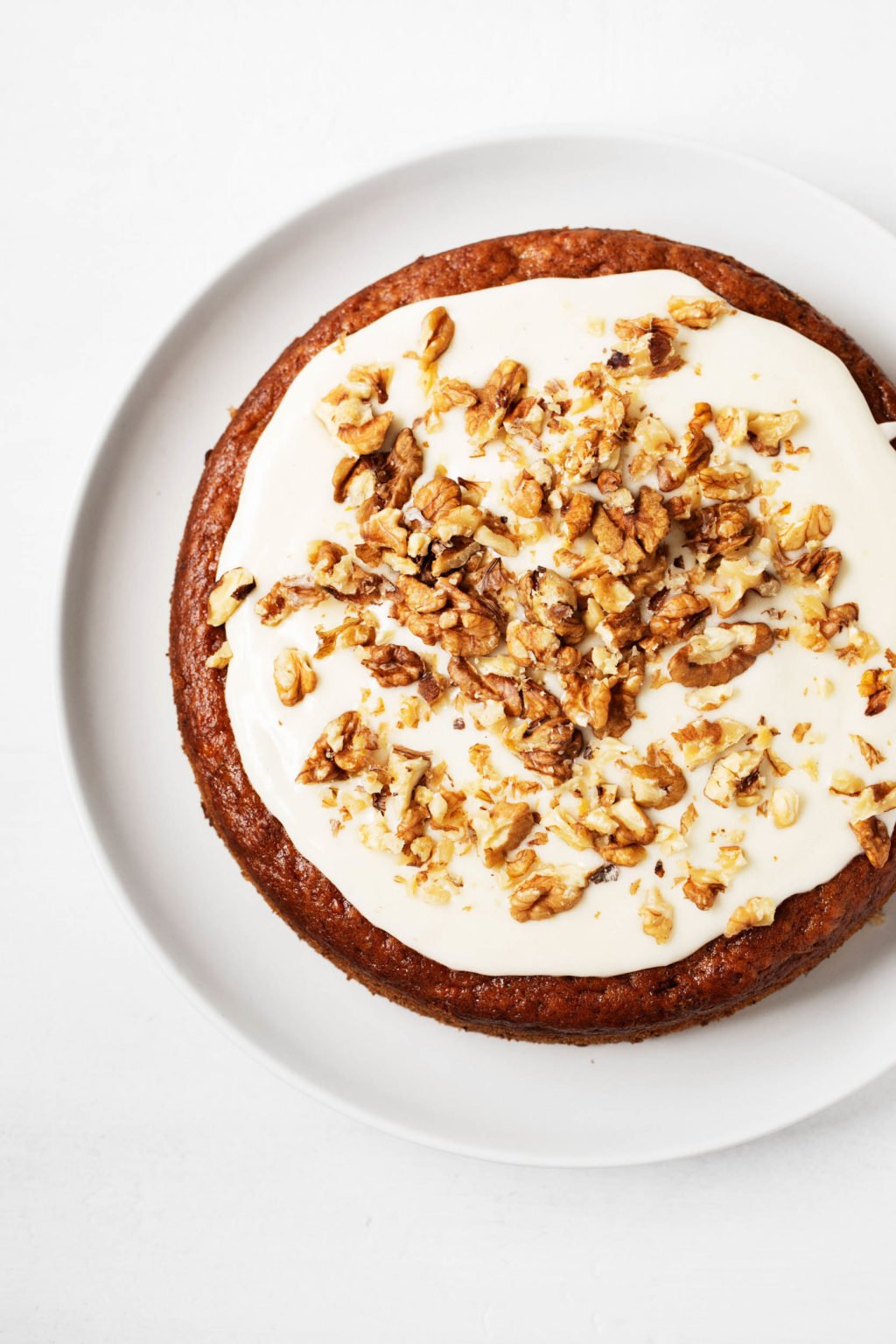 An overhead shot of a round, frosted cake with chopped walnuts.
