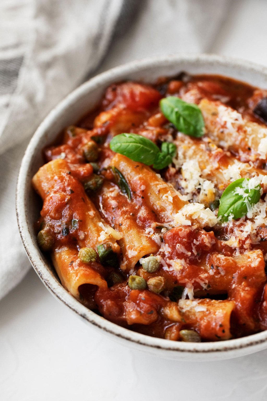 A angled photograph of a tomato and eggplant based pasta dish, which has been prepared with rigatoni and topped with small basil leaves.
