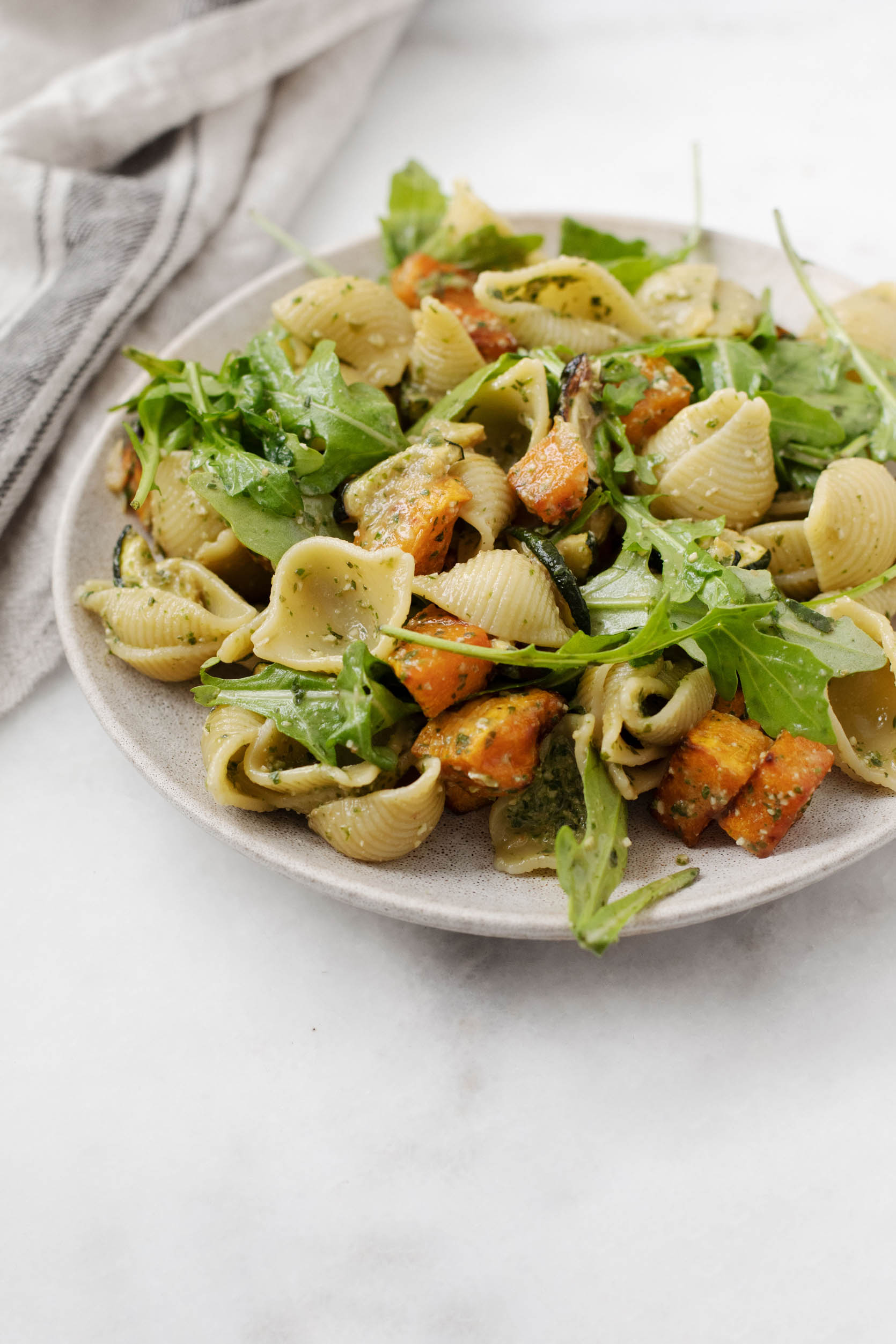 Roasted winter squash and zucchini are mixed with pasta and fresh arugula, along with pesto sauce, for a colorful plate of food.