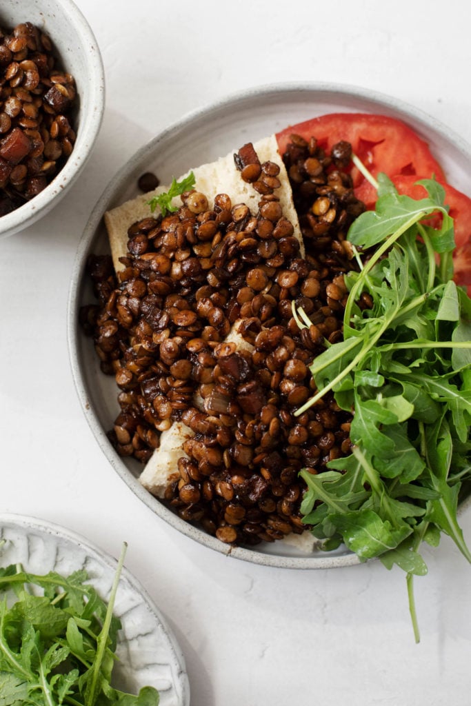 An overhead shot of sliced toast with red wine braised lentils and fresh arugula.