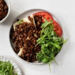 An overhead shot of red wine braised lentils on toast, served with greens and tomato.