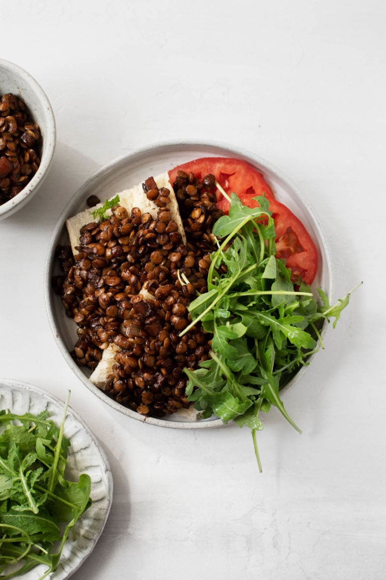 An overhead shot of red wine braised lentils on toast, served with greens and tomato.