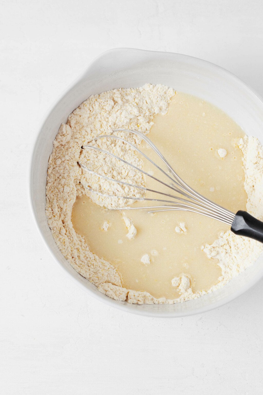 An overhead image of waffle batter, being mixed in a large white mixing bowl.